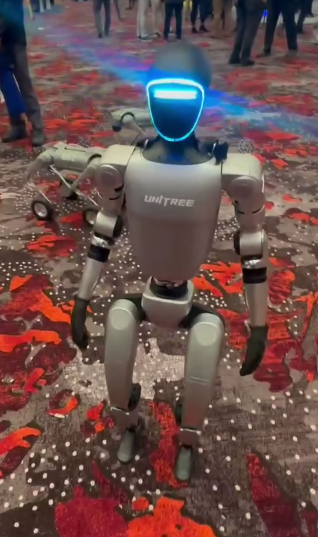 A small dark gray humanoid robot standing at a trade show