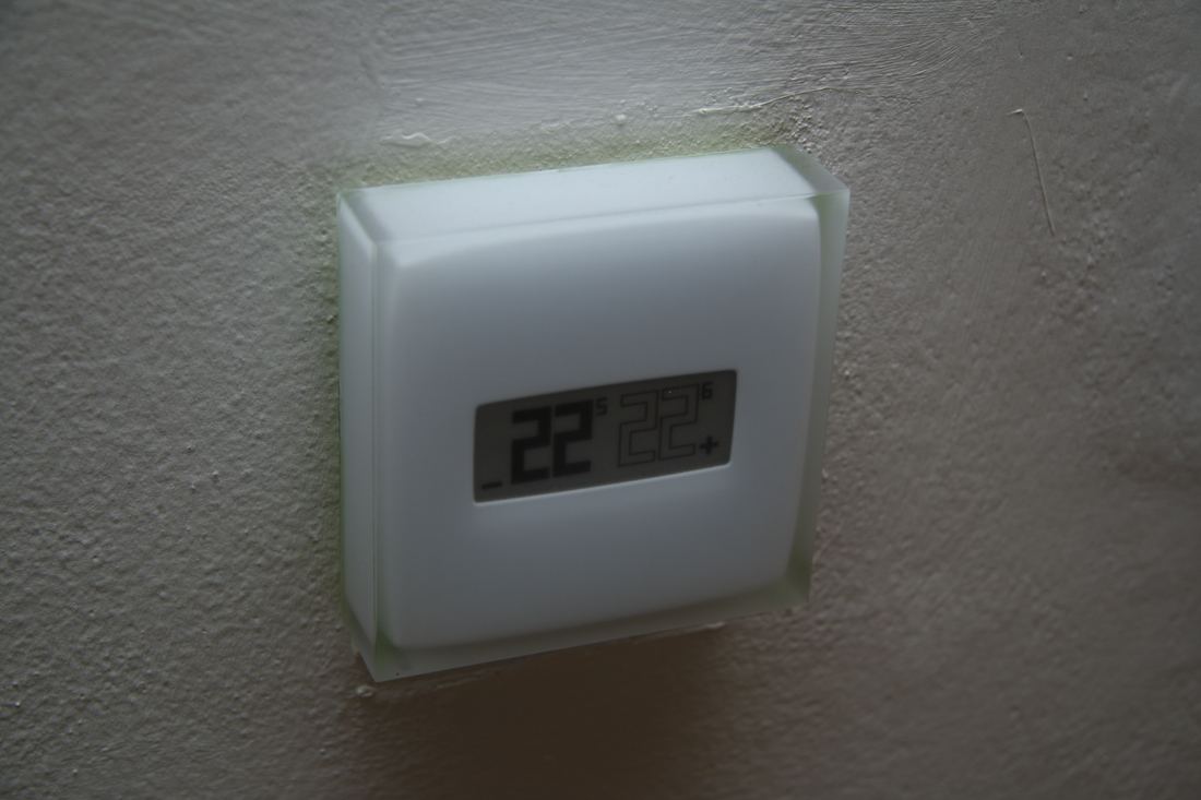 A small square smart thermostat mounted on a living room wall